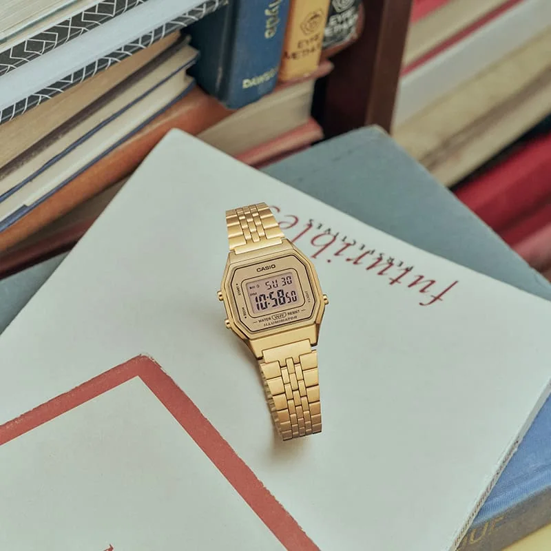 Die kleine goldene CASIO Vintage Collection Digitaluhr LA680WGA-9 wird auf Bücher und Studienmaterialien gelegt.