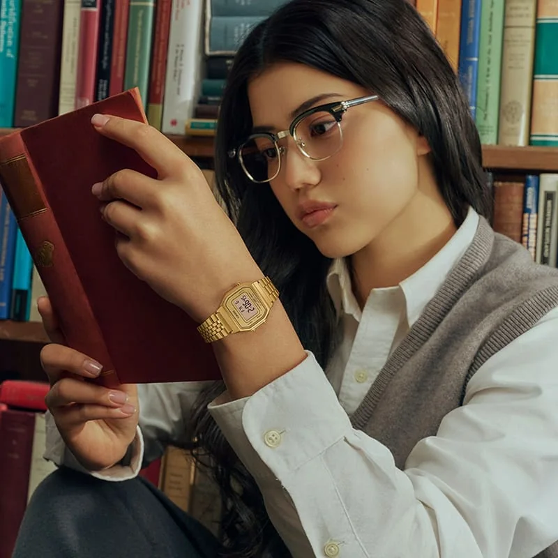 Eine Frau mit braunem Haar und Brille hält ein Buch und trägt die digitale CASIO Vintage Collection Uhr LA680WGA-9.