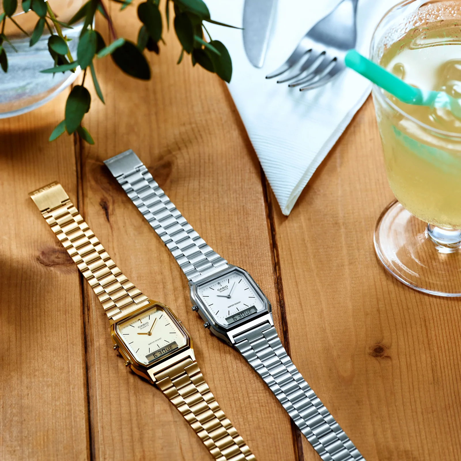 Die goldene AQ-230GA Armbanduhr liegt neben der silbernen Variante auf einem Holztisch.