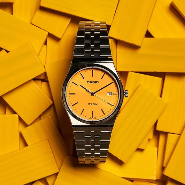 Die CASIO TIMELESS COLLECTION Armbanduhr MTP-B145D-9AV dekorativ platziert vor leuchtend gelben Täfelchen.