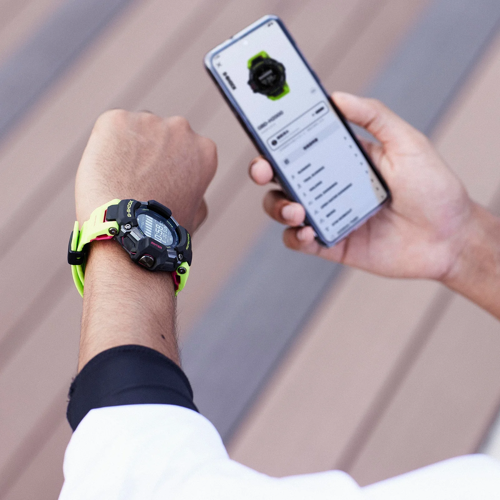 Eine Person trägt die Multisport-Uhr GBD-H2000-1A9 am linken Handgelenk während sie in der rechten Hand ein Smartphone hält, auf dem die übertragenen Daten der Uhr zu sehen sind