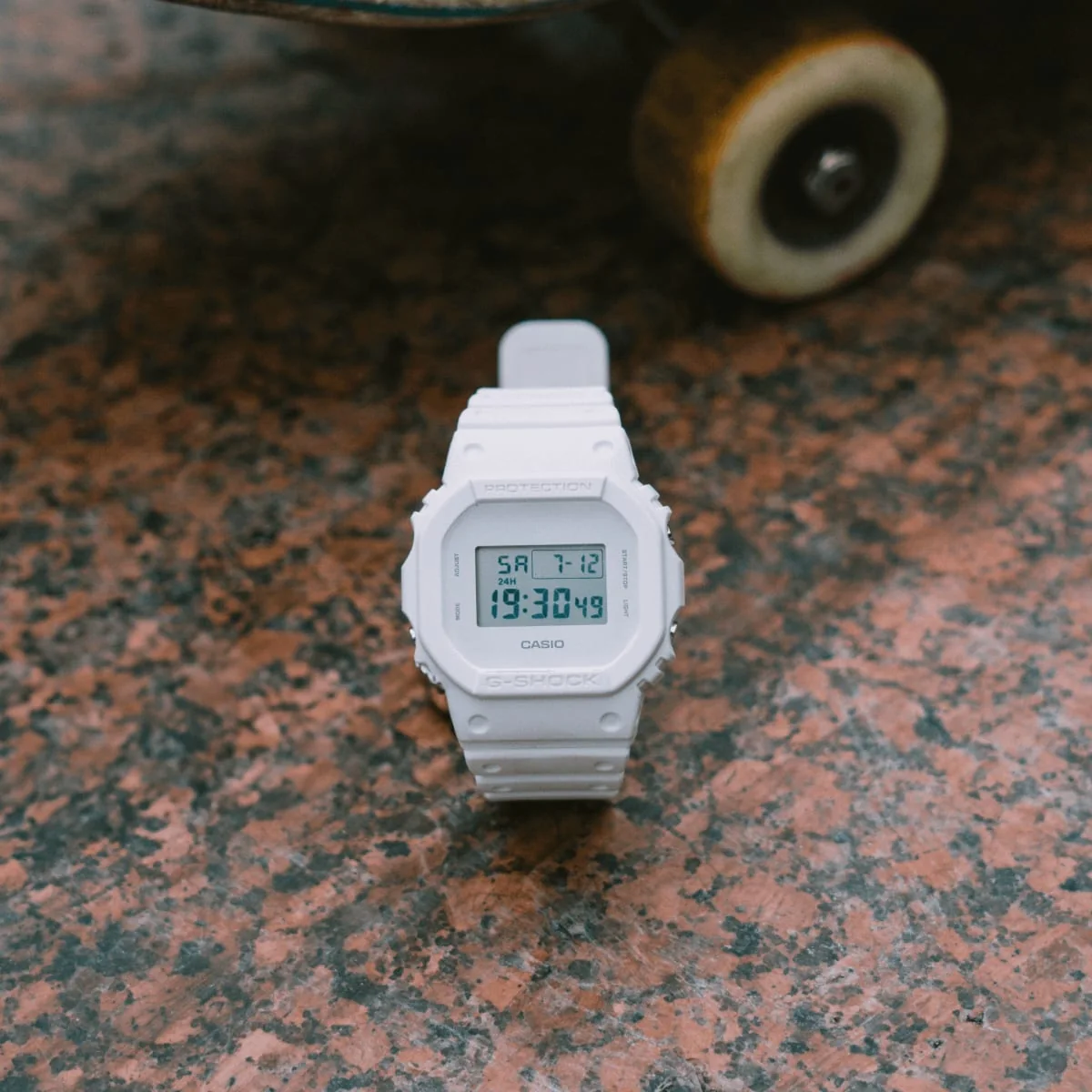 Frontansicht der DW-5600WW-7 auf einem rötlichen Steinboden. Im Hintergrund ist ein Skateboard zu sehen