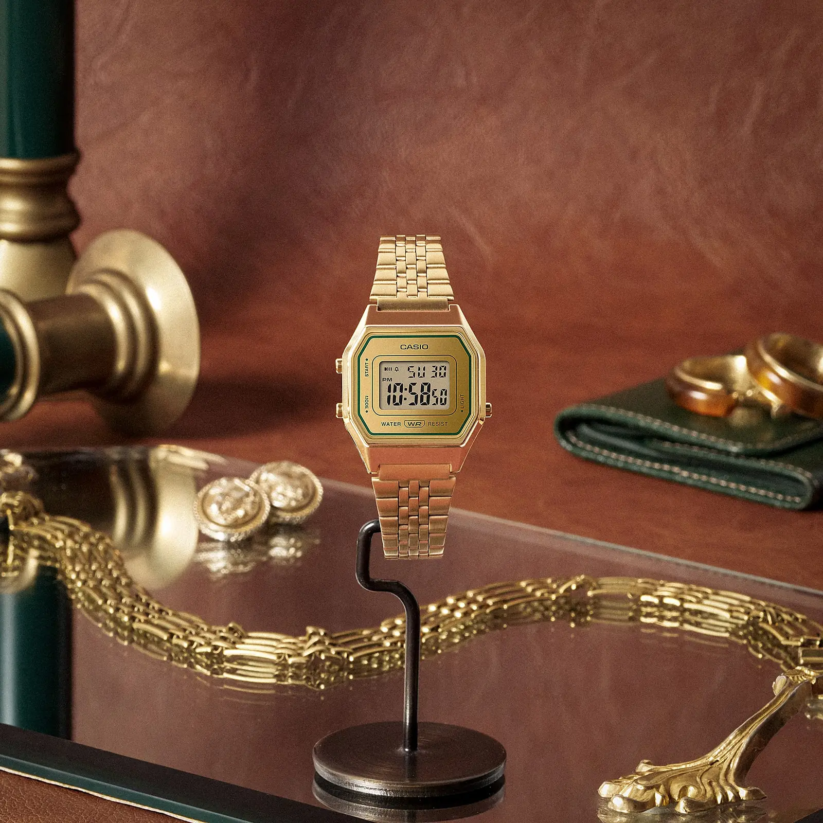 Die CASIO VINTAGE COLLECTION Armbanduhr LA680WEGV-9A ,drapiert auf einem Tisch mit Goldschmuck und Accessoires.