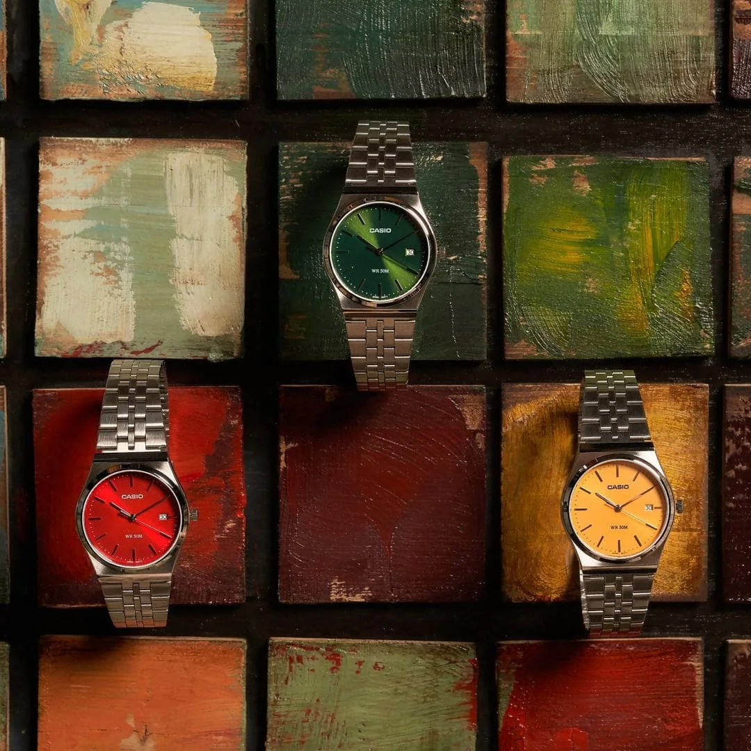 Die CASIO TIMELESS COLLECTION Armbanduhr MTP-B145D-9AV neben zwei ähnlichen Modellen mit rotem bzw. grünem Zifferblatt.