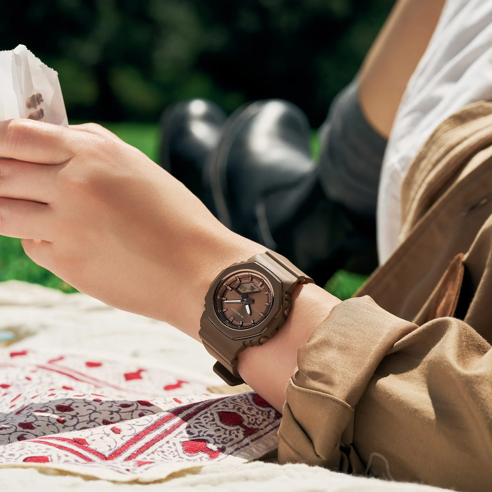 Eine Frau liegt draußen auf einer Picknickdecke und trägt die Armbanduhr GMA-P2110B-5AER von G-SHOCK am Handgelenk