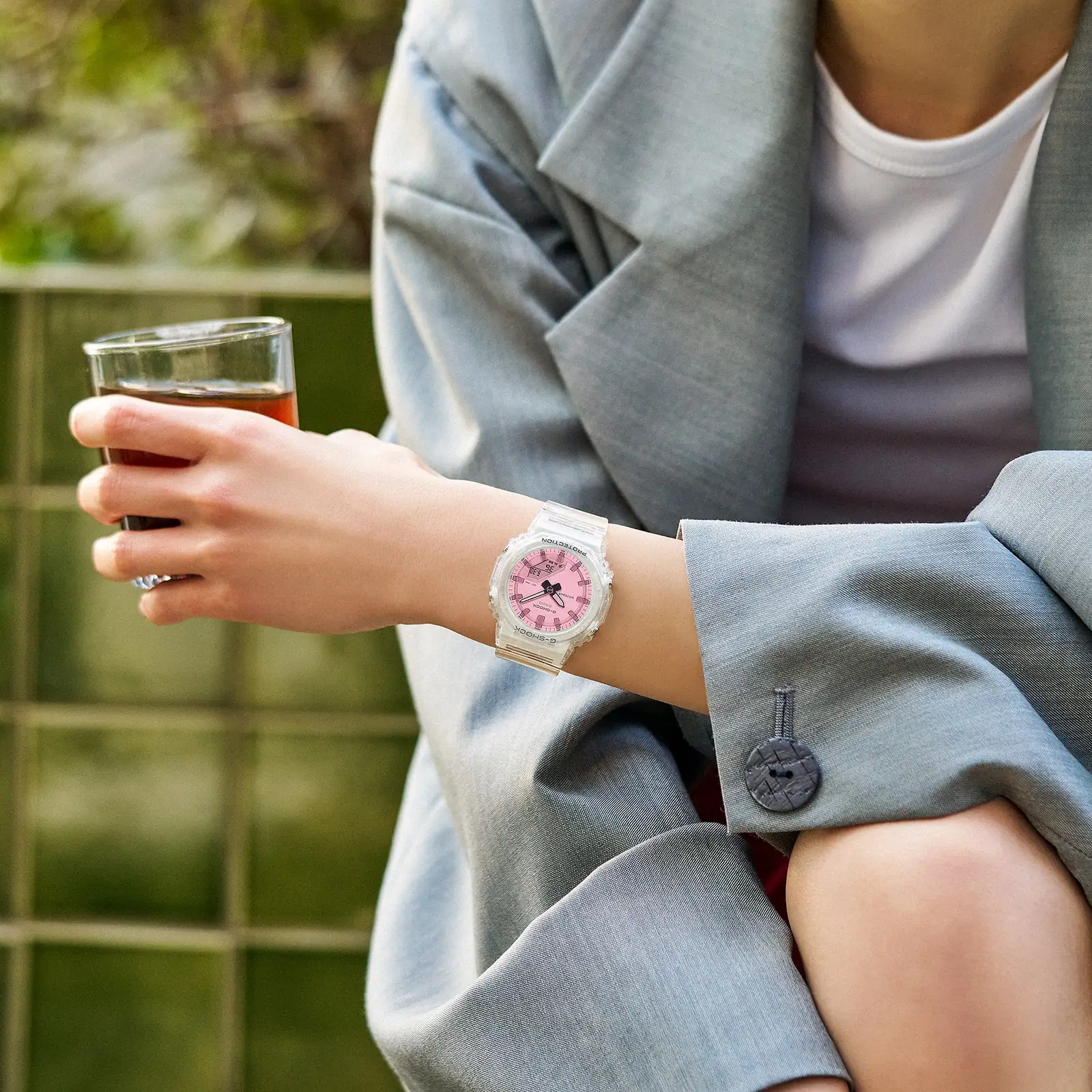 Eine Frau mit einem grauen Oversize-Blazer trägt die G-SHOCK Armbanduhr GMA-P2100SR-7AER am Handgelenk