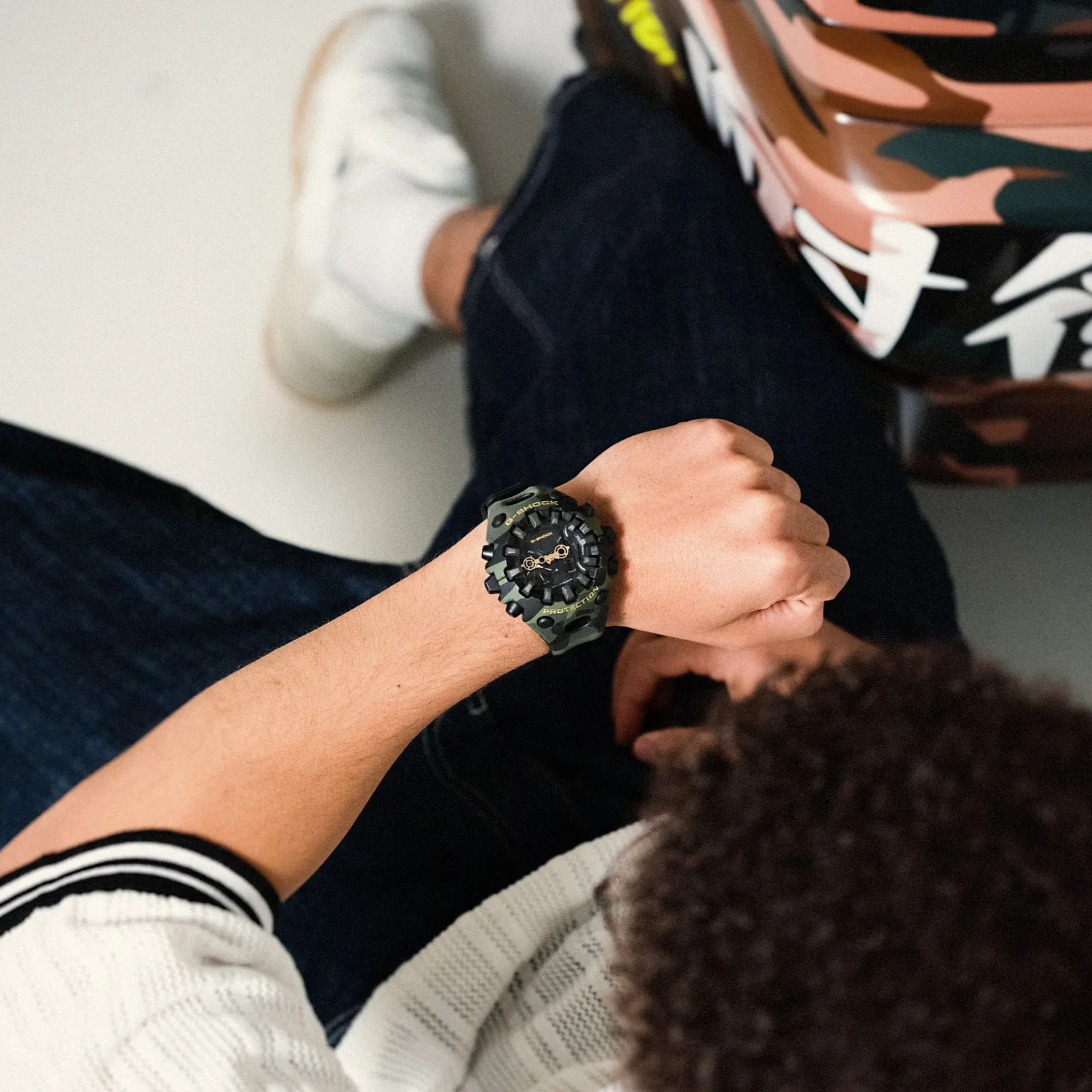 Ein Mann in Jeans schaut auf sein Handgelenk, an dem er die Camouflage Armbanduhr GA-V01CMG-3AER von G-SHOCK trägt
