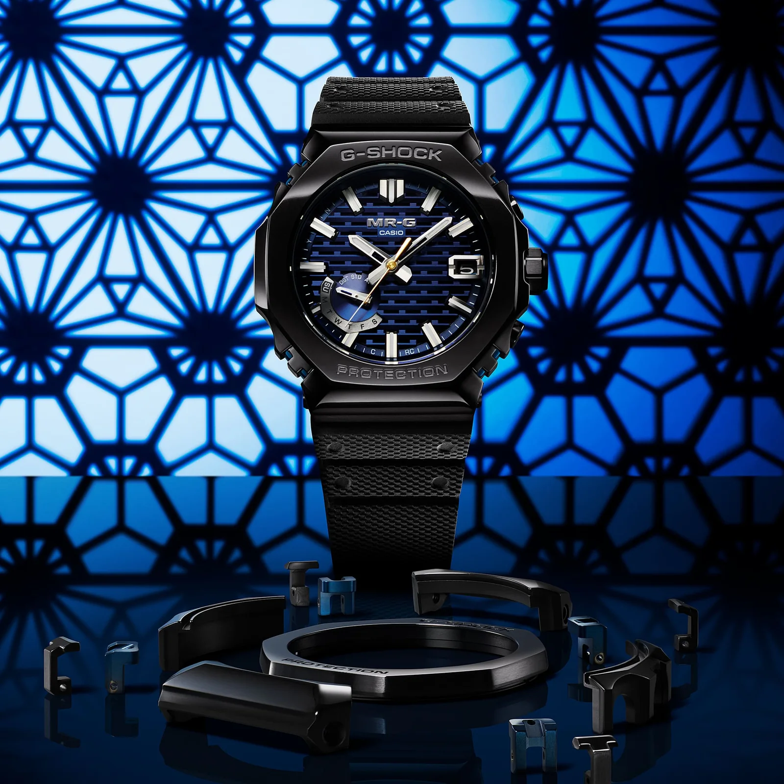 Die schwarze Analoguhr MRG-B2100R-2A mit dunkelblau-gemustertem Zifferblatt vor einem blau-schwarz gemustertem Hintergrund