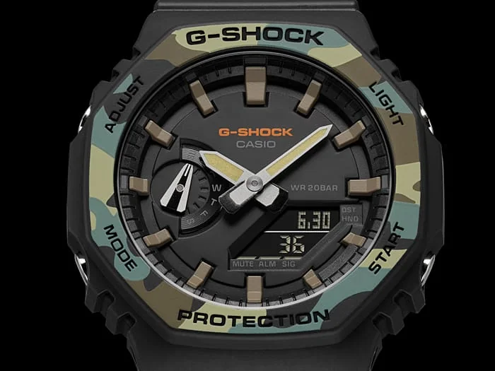 Nahaufnahme des digital-analogen Zifferblatts der G-SHOCK Armbanduhr GA-2100SU-1A in Schwarz mit graubeigen Indices und einer Lünette in Camouflage-Optik in Grüntönen.