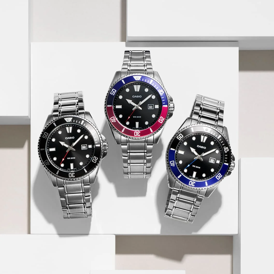 Die CASIO TIMELESS COLLECTION Armbanduhr MDV-107D-1A1V neben den beiden ähnlichen Modellen mit blauroter bzw. schwarzblauer Lünette.
