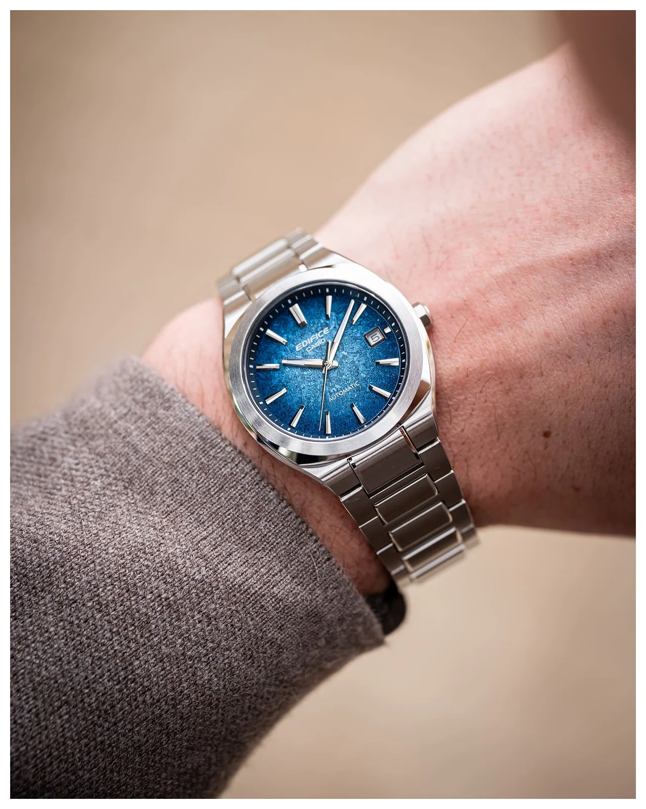Ein Mann mit einem grauen Oberteil trägt die mechanische Armbanduhr EFK-200D-2AER von EDIFICE am Handgelenk