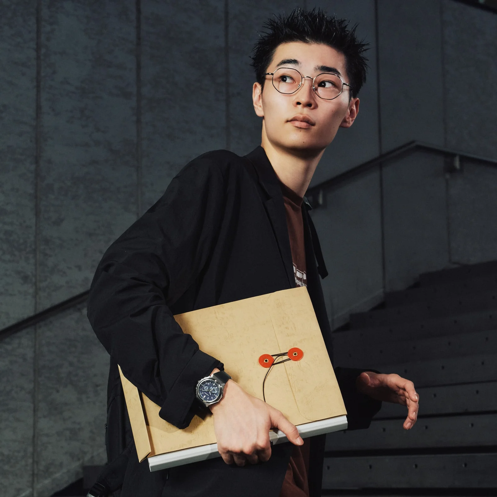 Ein Mann mit einem schwarzen Hemd trägt Dokumente unter dem Arm und die GST-B1000-2AER von G-SHOCK am Handgelenk