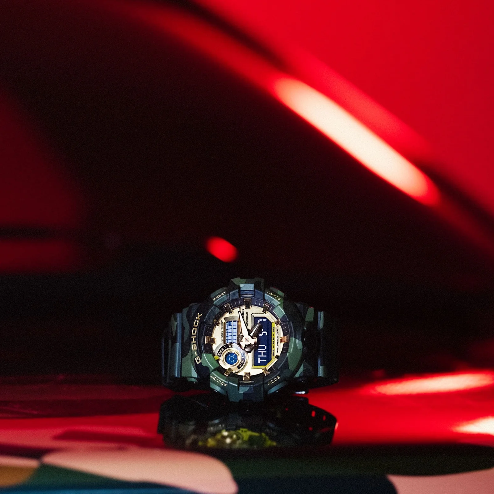 Die Armbanduhr GA-700CMG-3AER liegt auf einer Rot glänzenden Oberfläche