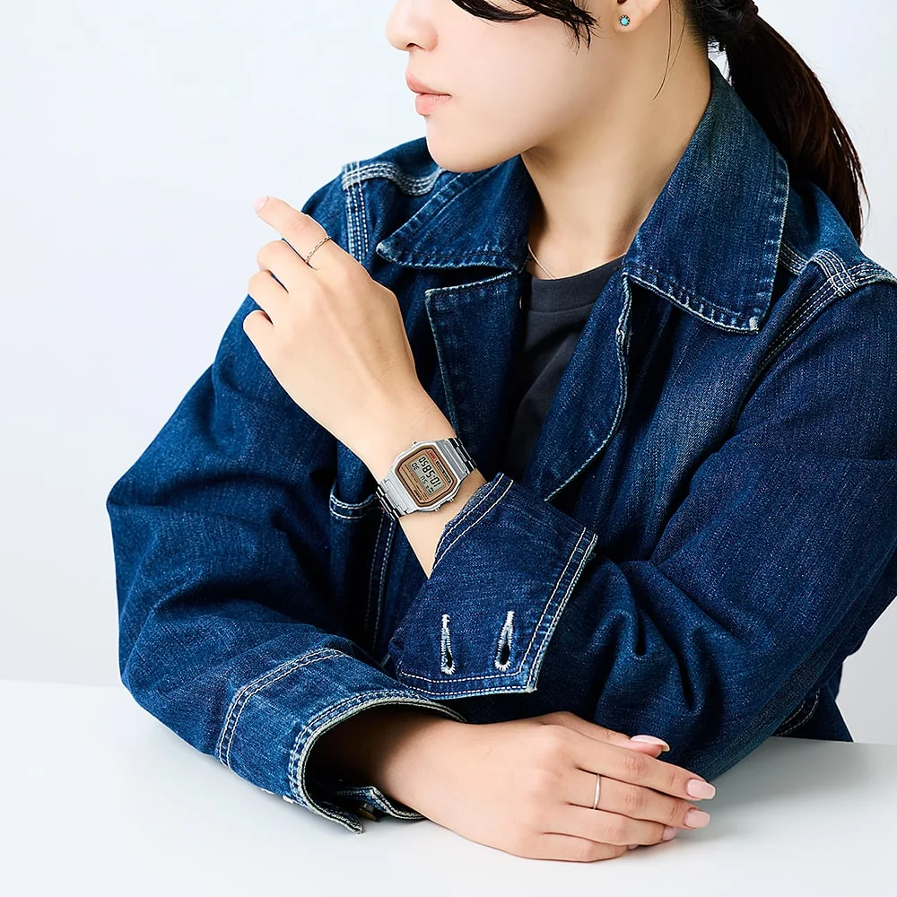 Frau in Jeansjacke mit Ringen trägt A158WEA-9 Digitaluhr am Handgelenk und lehnt entspannt an einem weißen Tisch