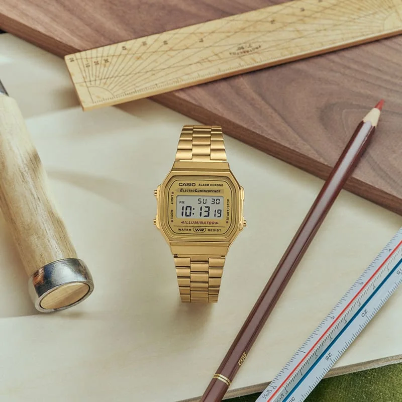 Die CASIO Vintage Collection Uhr A168WG-9 mit goldenem Band und digitaler Anzeige wurde mit Werkzeugen und Schreibwaren platziert.