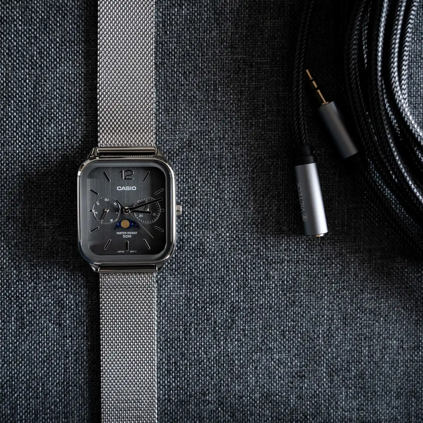 Ansicht der flach liegenden CASIO TIMELESS COLLECTION Armbanduhr MTP-M305M-8AV auf grauem Textiluntergrund neben einem in grauem Textil ummantelten Verlängerungskabel.