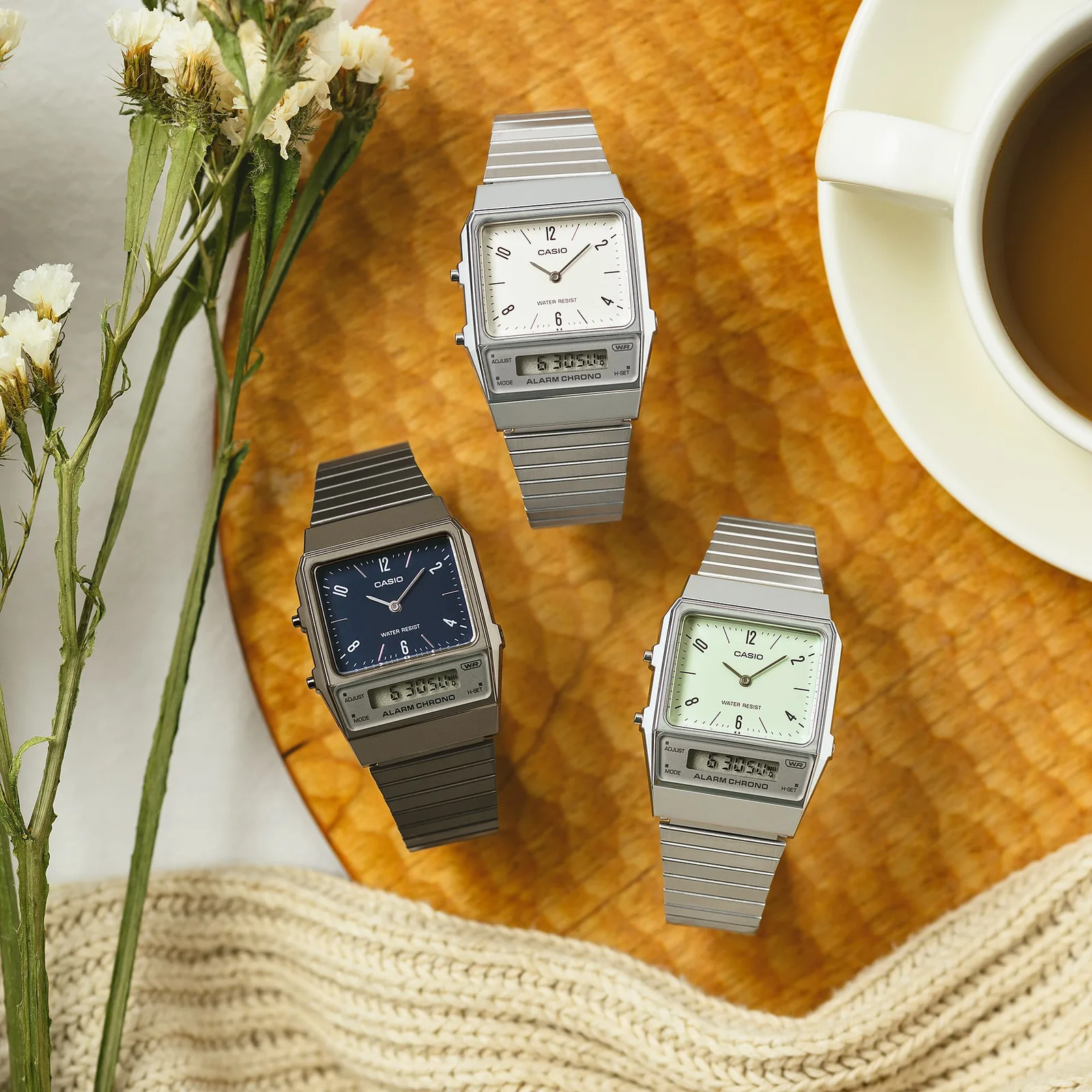Auf einem Tisch liegen die drei Modelle AQ-800EB-2A, AQ-800E-7A2, AQ-800E-3A neben einer Kaffeetasse und einer Blume