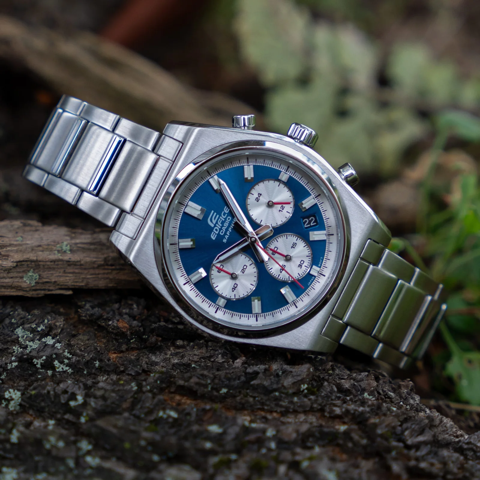 Seitliche Ansicht der liegenden EDIFICE Armbanduhr EFB-730D-2AVU mit blauem, analogem Zifferblatt, rotem Sekundenzeiger, Hilfszifferblättern in Silber mit roten Zeigern sowie einem Gehäuse und Armband aus massivem Edelstahl in Silber.