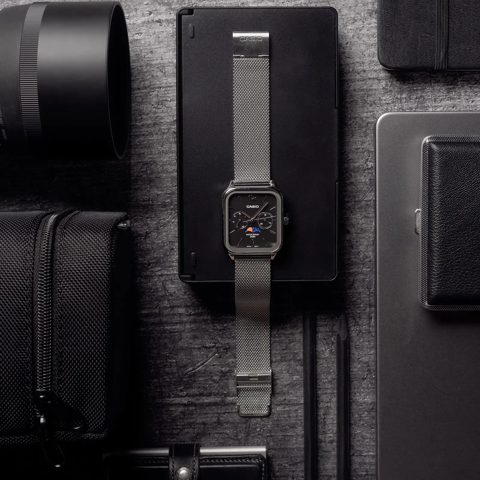 Komplettansicht der flach liegenden CASIO TIMELESS COLLECTION Armbanduhr MTP-M305M-1AV inmitten verschiedener Schreibtisch- und Fotografie-Utensilien.