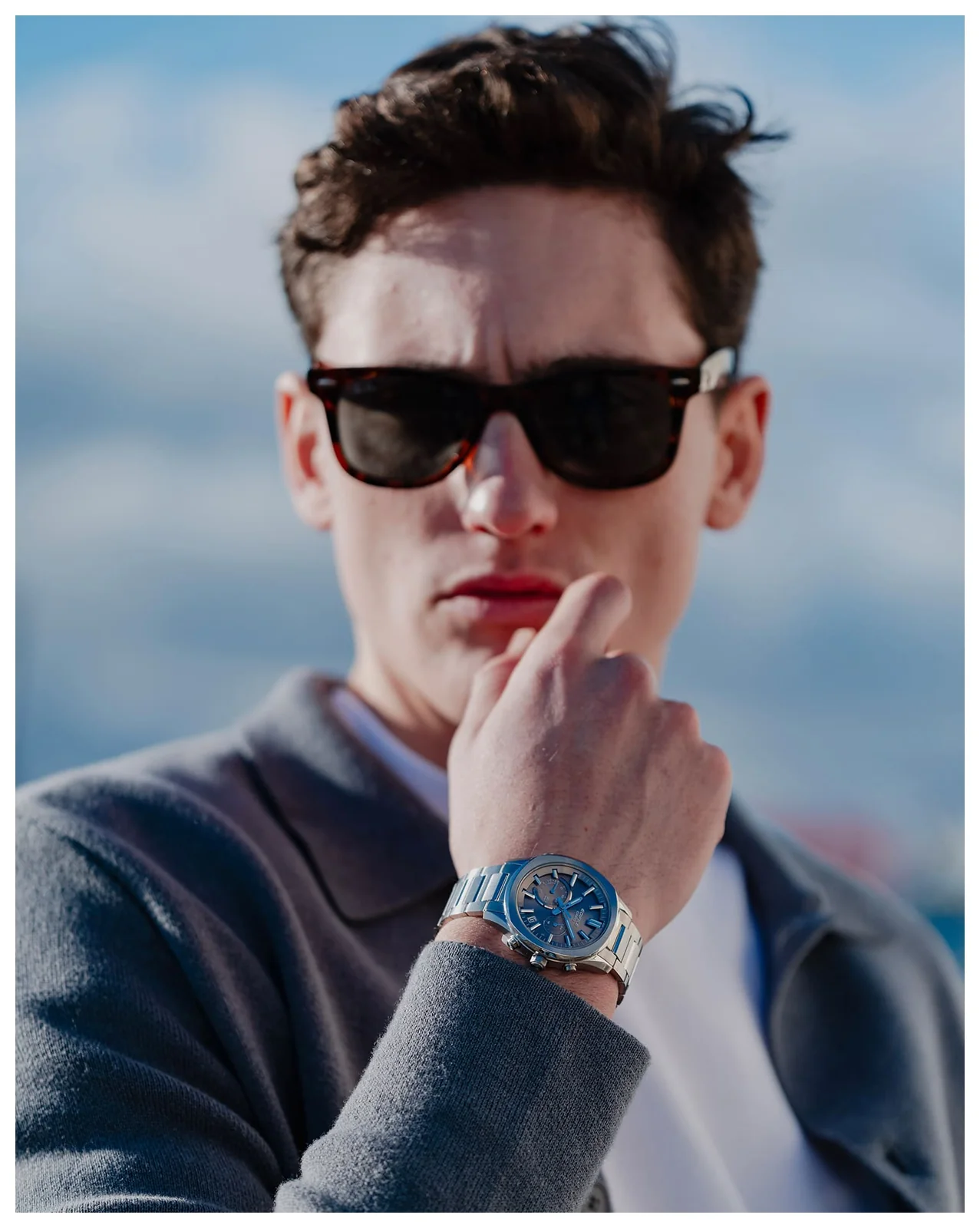 Ein Mann mit einer grauen Sweatshirt Jacke und einer Sonnenbrille trägt die EDIFICE Armbanduhr EQB-1300D-5AEF am Handgelenk