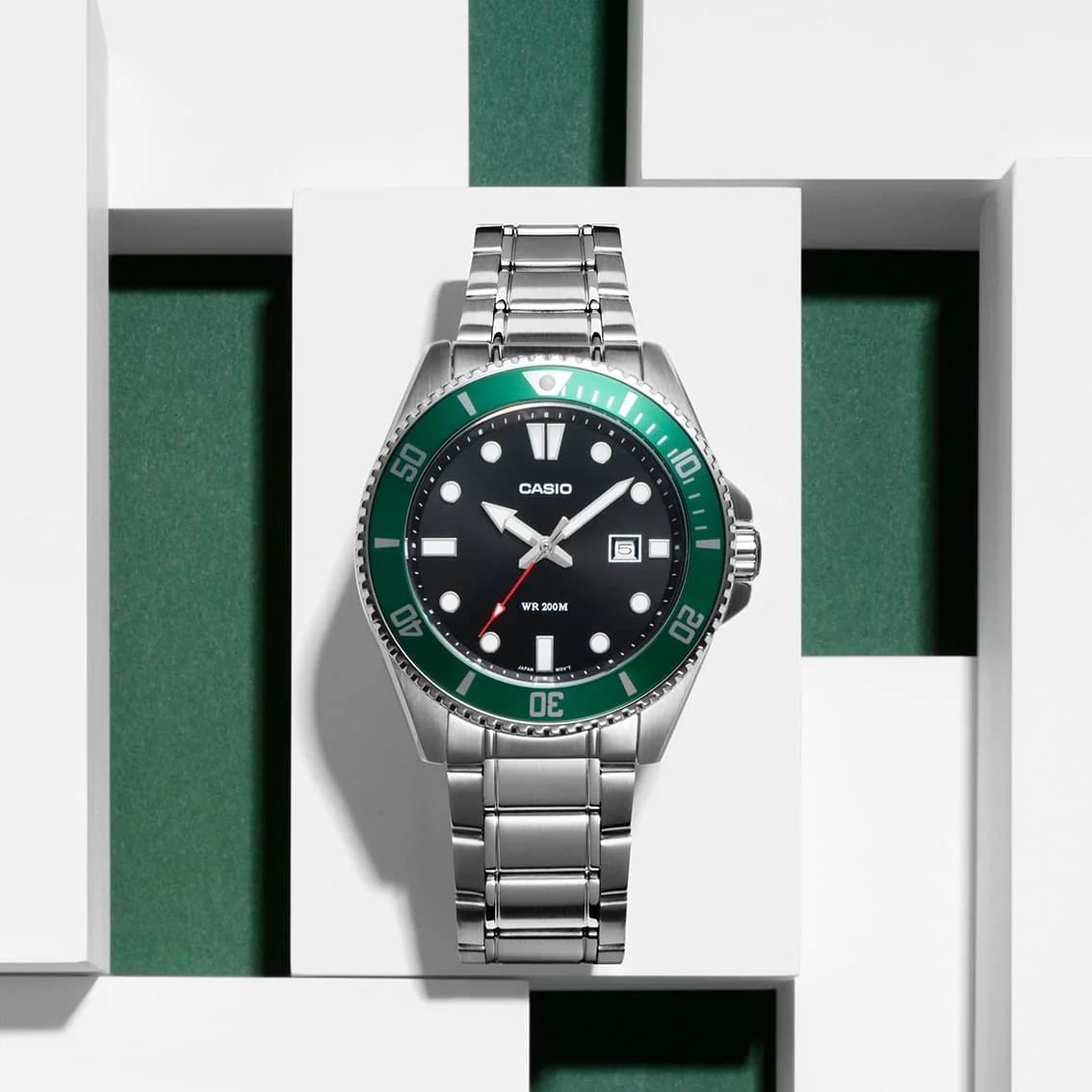 Die CASIO TIMELESS COLLECTION Armbanduhr MDV-107D-3AV von vorn, platziert vor einem dekorativen Hintergrund aus weißen und grünen Blöcken.