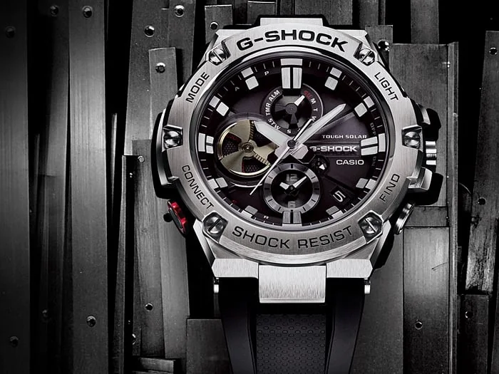 Nahaufnahme des analogen Zifferblatts der G-SHOCK Armbanduhr GST-B100-1A vor Metallelementen.