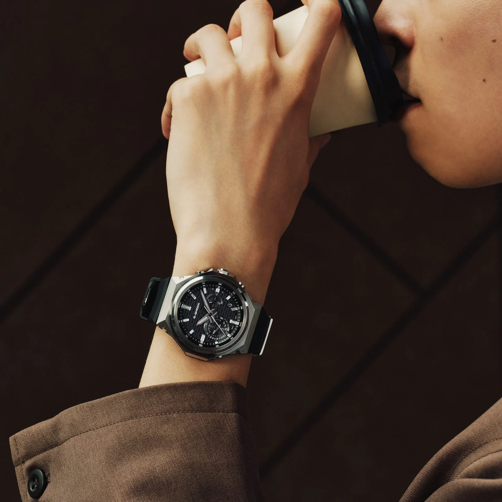 Ein Mann trinkt aus einem Kaffeebecher und trägt die schwarze GST-B1000-1AER am Handgelenk