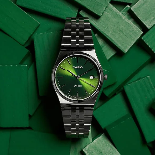 Die CASIO TIMELESS COLLECTION Armbanduhr MTP-B145D-3AV dekorativ drapiert auf einer unsortierten Menge grüner Täfelchen.