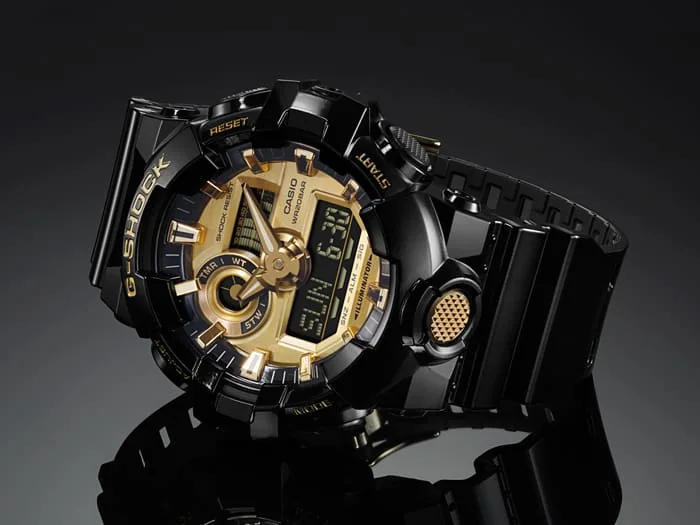 Die seitlich liegende G-SHOCK Armbanduhr GA-710GB-1A mit goldener Bedientaste vorn.